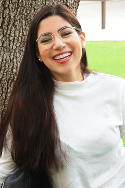 Mariana, a UTSA student, sits in front of a tree on UTSA's campus