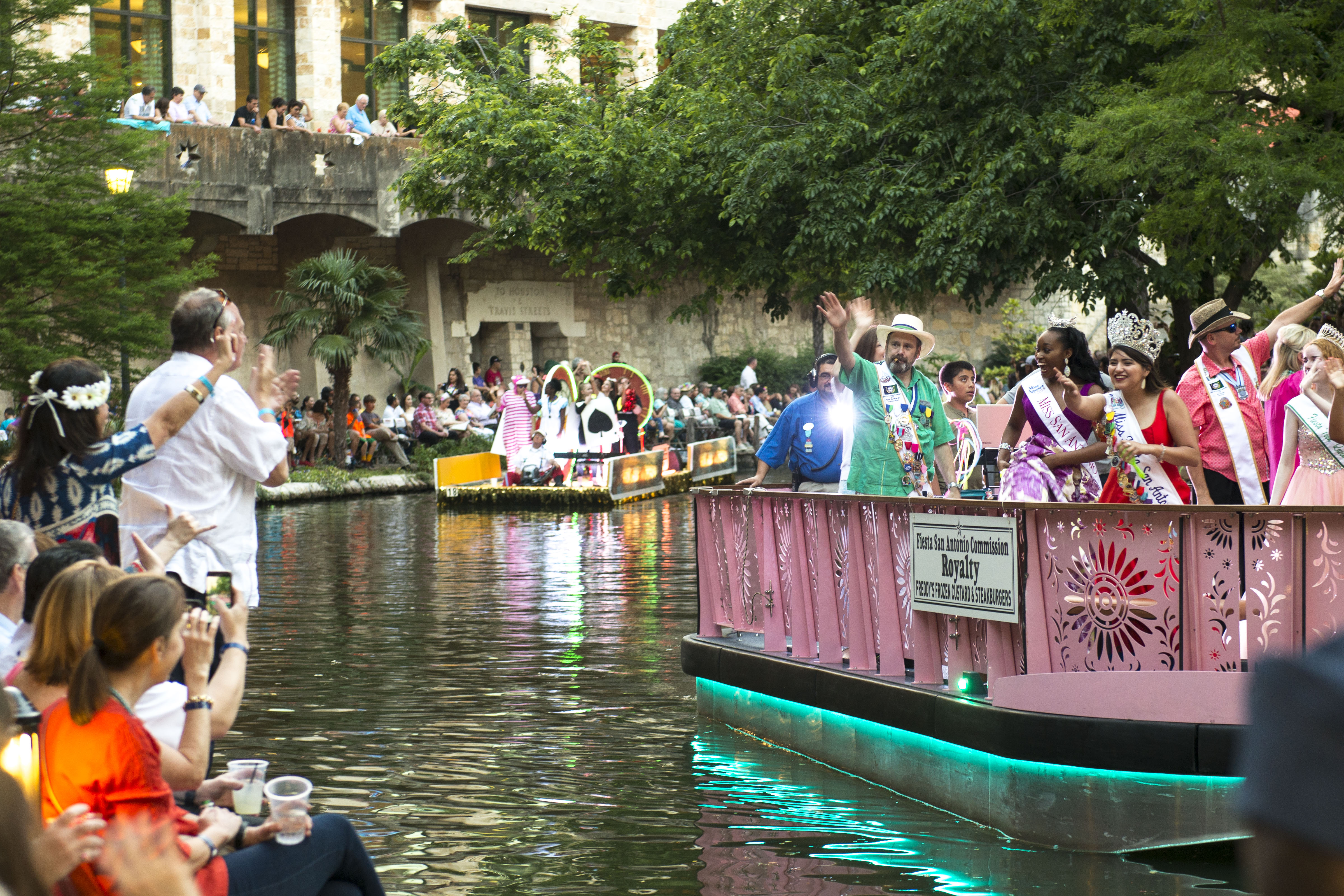 Crowds applauding during a river boat parade in the San Antonio river