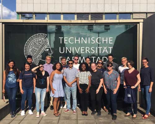 A group of people standing in front of a glass wall displaying the "Technische Universität Darmstadt" logo.